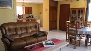 Ein Wohnzimmer mit braunem Ledersofa, einem Holzesstisch mit Stühlen und einer Küche im Hintergrund.