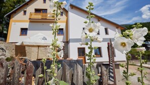 Un edificio di due piani con un balcone, una recinzione in legno e fiori bianchi in primo piano.