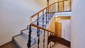 Una scala con ringhiera in legno e balaustre nere, che porta a un pianerottolo con una porta e una piccola finestra.