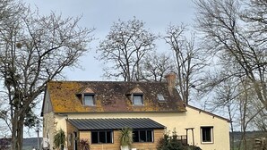 Une maison à deux étages, dotée d’un toit en pente, d’un petit porche et d’un étang à l’avant.