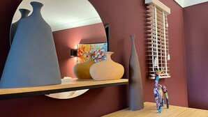 Une pièce dotée d’un grand miroir qui reflète des vases et un tableau, d’une table en bois et d’une fenêtre avec des stores.