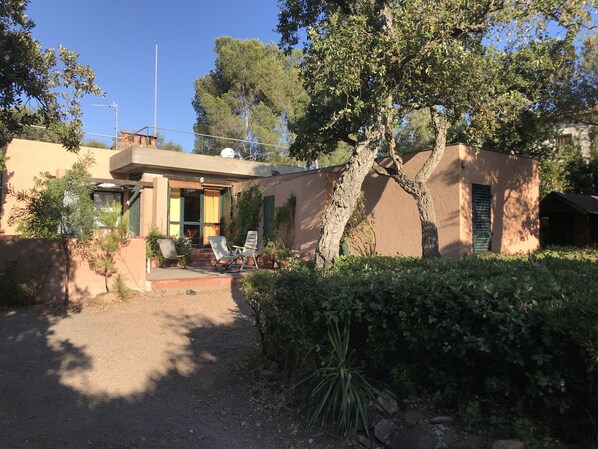 A single-story house with a patio area, a small garden, and a tree in front.