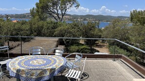 A terrace with a table and chairs, overlooking a scenic coastal landscape with trees and a view of the sea.