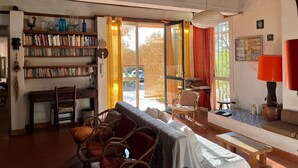 A spacious living room with a bookshelf, a sofa, a dining table, and a large window with curtains.