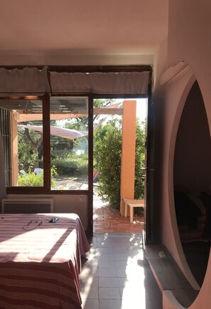 A bedroom with a bed, a window, and a view of an outdoor patio area.