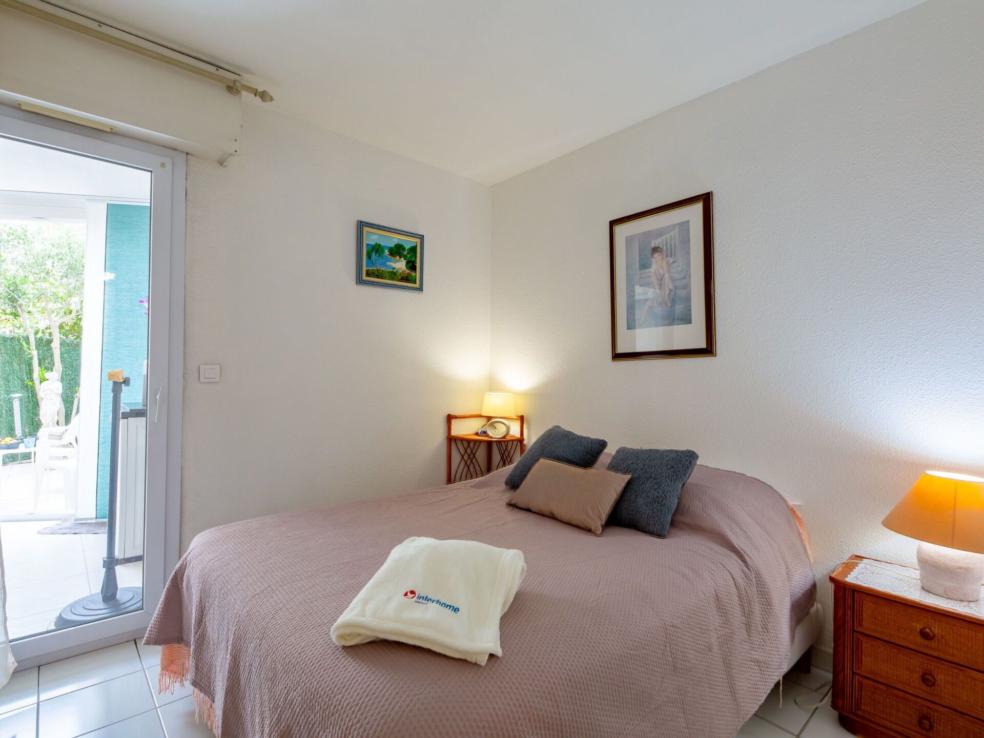 A bedroom with a bed, a nightstand, a lamp, and a window.