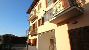 A multi-story residential building with a balcony, a staircase leading to the entrance, and a gated driveway.
