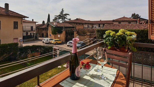 A balcony with a table set for two, featuring a bottle of champagne, a bowl of strawberries, and two wine glasses.