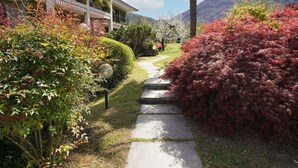 Ein Weg führt zu einem Gebäude mit Balkon, umgeben von üppigem Grün und einer Bergkulisse.