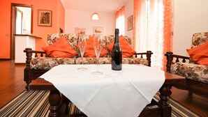 Ein Zimmer mit einer blumigen Couch, einem Holztisch mit weißer Tischdecke und einer Champagnerflasche.