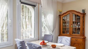 Un coin repas avec une table dressée pour quatre personnes, un buffet en bois doté de portes en verre et une fenêtre ornée de rideaux blancs.