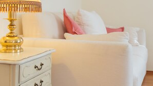 Ein ordentlich eingerichtetes Schlafzimmer mit einem weißen Bett, einem Nachttisch mit Lampe und zwei gerahmten Bildern an der Wand.