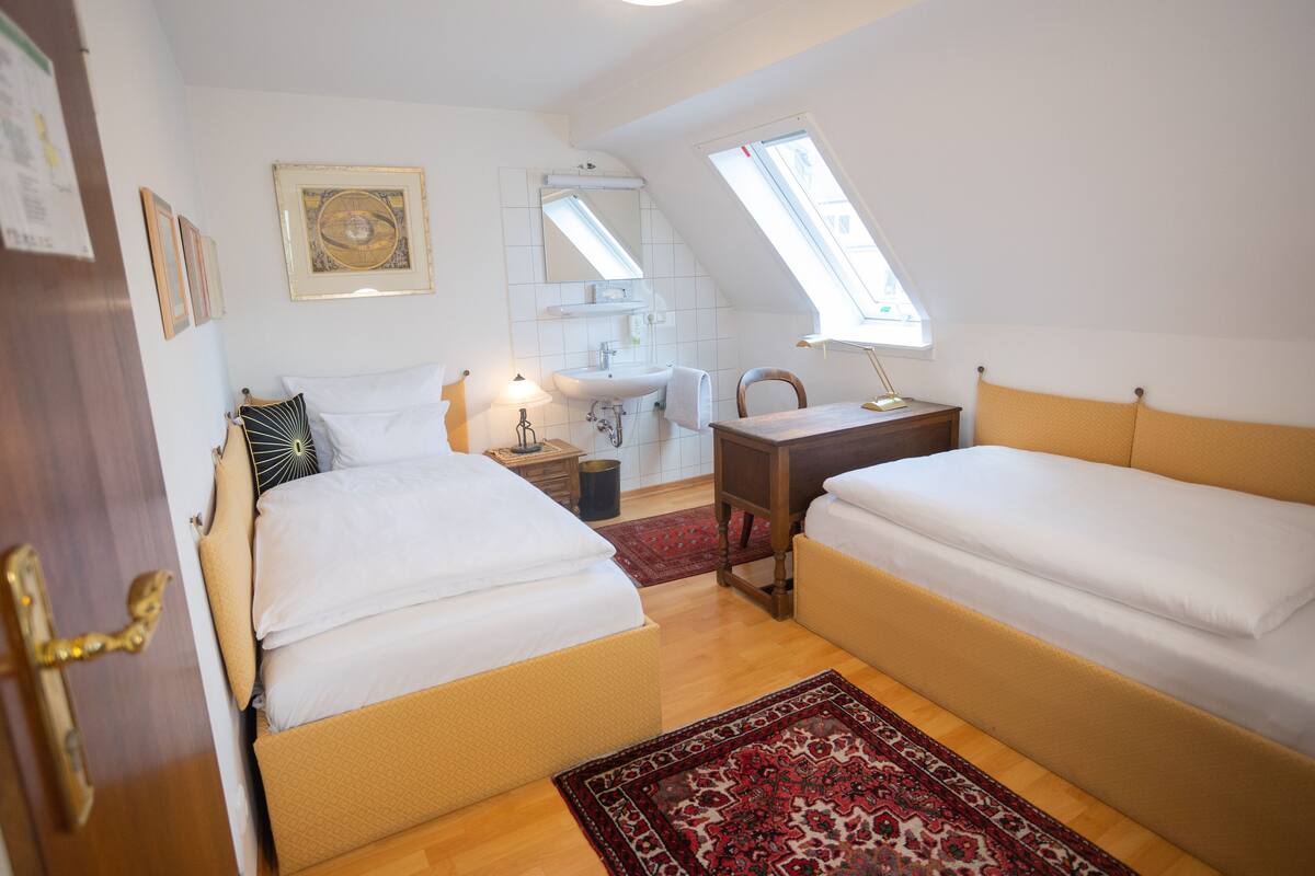 A bedroom with two beds, a desk, a sink, and a window.