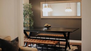 A dining area with a dark wooden table, two cushioned benches, a potted plant, and a large mirror with hanging lights. - Cozy 3BR Home with AC, Hot Tub & Walkable Restaurants (Wheat Ridge)