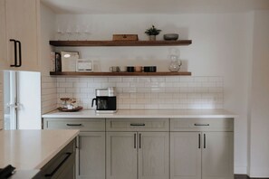 A kitchen with white tiles, a coffee maker, and wooden shelves.