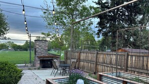 An outdoor patio area with a brick fireplace, metal chairs, and a wooden fence. - Cozy 3BR Home with AC, Hot Tub & Walkable Restaurants (Wheat Ridge)