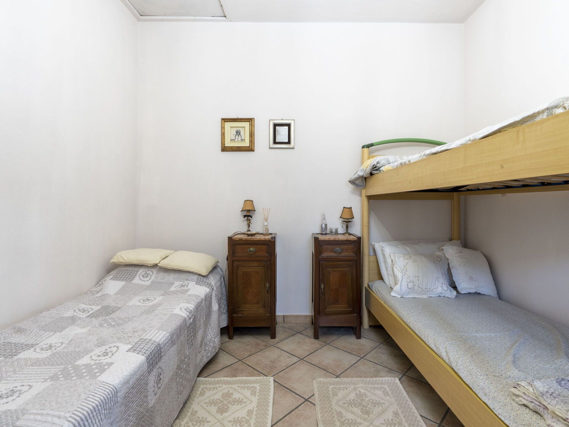 Ein kleiner, kompakter Raum mit zwei Einzelbetten, einem Hobbeltbett und einem kleinen Nachttisch mit Lampen sowie einem Holzschrank.