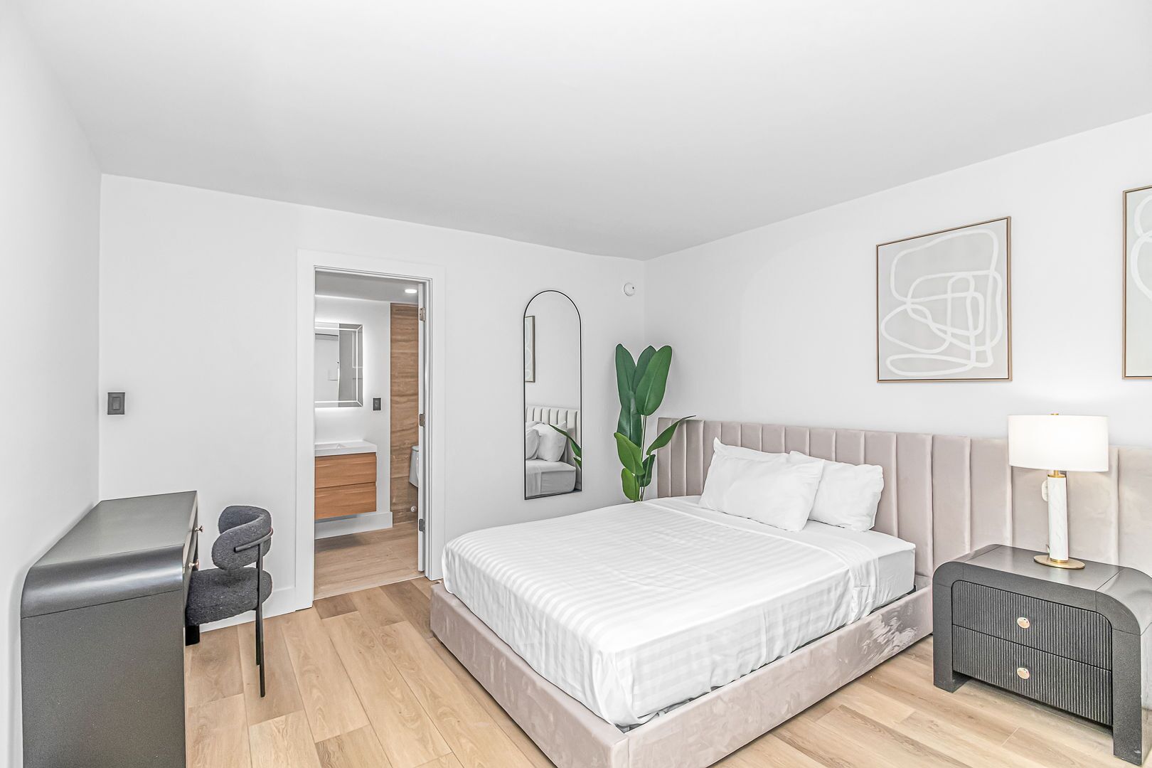 A modern bedroom with a large bed, bedside tables, a desk, and a mirror.