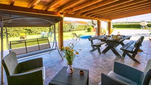 Une terrasse extérieure avec des poutres en bois, des meubles en osier et une vue sur un jardin.