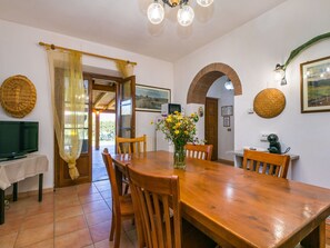 A dining area with a wooden table, chairs, a vase of flowers, and a television on a table.