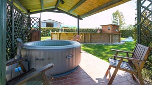 A covered patio area with a hot tub, wooden deck, and outdoor seating.