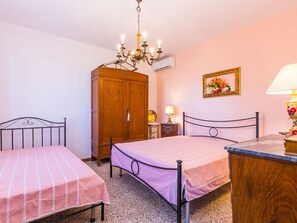 Une chambre avec deux lits, une armoire en bois, un lustre, une table de chevet avec une lampe et un tableau encadré au mur.