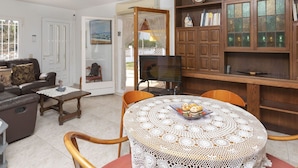 A living room with a sofa, a coffee table, a dining table with a lace tablecloth, and a wooden cabinet with glass doors. - Wonderful  villa for 6 people with WIFI and TV (L'escala)