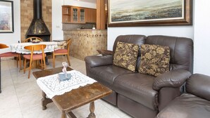 A living room with a leather sofa, a dining table with chairs, a fireplace, and a kitchen area. - Wonderful  villa for 6 people with WIFI and TV (L'escala)