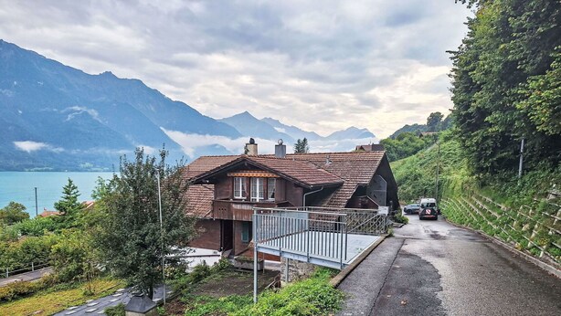 Eine rustikale Chalet mit geneigtem Dach, einer Holzdiele und Blick auf einen See und Berge.