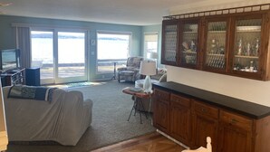 A living room with a sofa, a TV, a dining table, and a cabinet. - M-22 Lakefront Property in Onekama with amazing Sunsets!! (Onekama)