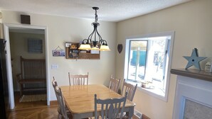 A dining area with a wooden table and chairs, a chandelier, a window with a view, and a fireplace. - M-22 Lakefront Property in Onekama with amazing Sunsets!! (Onekama)