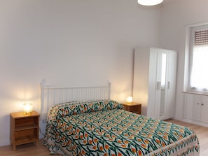 A bedroom with a bed, a wardrobe, a nightstand with a lamp, and a radiator. - Cosy apartment for 7 people with WIFI, TV, balcony and pets allowed (Rome)