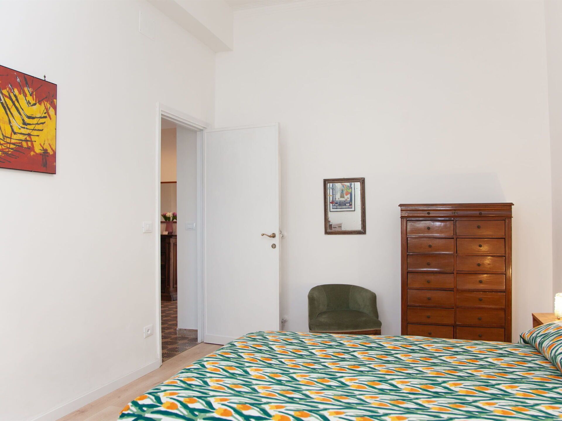 A bedroom with a bed, a dresser, a chair, and a door leading to another room.