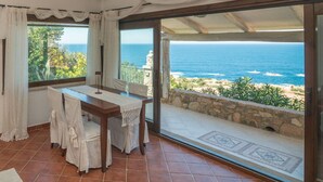 A room with a table and chairs, a view of the ocean, and a stone wall.