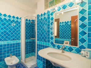 A bathroom with blue-tiled walls, a glass-enclosed shower, a sink, and a bidet.