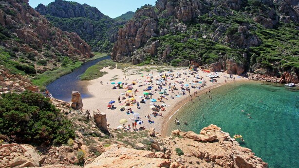 A coastal beach with rocky cliffs and clear waters.