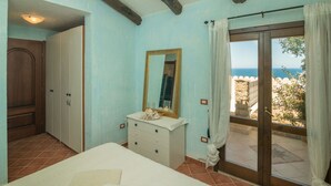 A bedroom with a bed, dresser, and a large mirror. There is a sliding glass door leading to an outdoor area with a view of the sea.