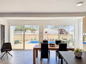 Un espace repas comprenant une table, des chaises et donnant sur une piscine et un jardin.