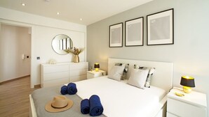 Un dormitorio moderno con una cama grande, mesitas de noche, un tocador, un espejo y cuadros en la pared.