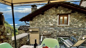 A stone building with a window, a table with a tablecloth, chairs, a bottle of wine, and a vase with flowers. - Beautiful private villa for 3 guests with WIFI, TV, terrace and pets allowed (Verceia)