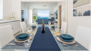 A modern dining area with a long table set for four, a bottle of wine, and a view of the cityscape through the window. - Cosy apartment for 4 guests with A/C, WIFI, TV and terrace (Terrasini)