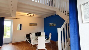 A dining area with a glass table and white chairs, a staircase with white railings, and a blue accent wall. - Nice apartment for 5 guests with WIFI, pool, TV and terrace (Saint-jouan-des-guérets)