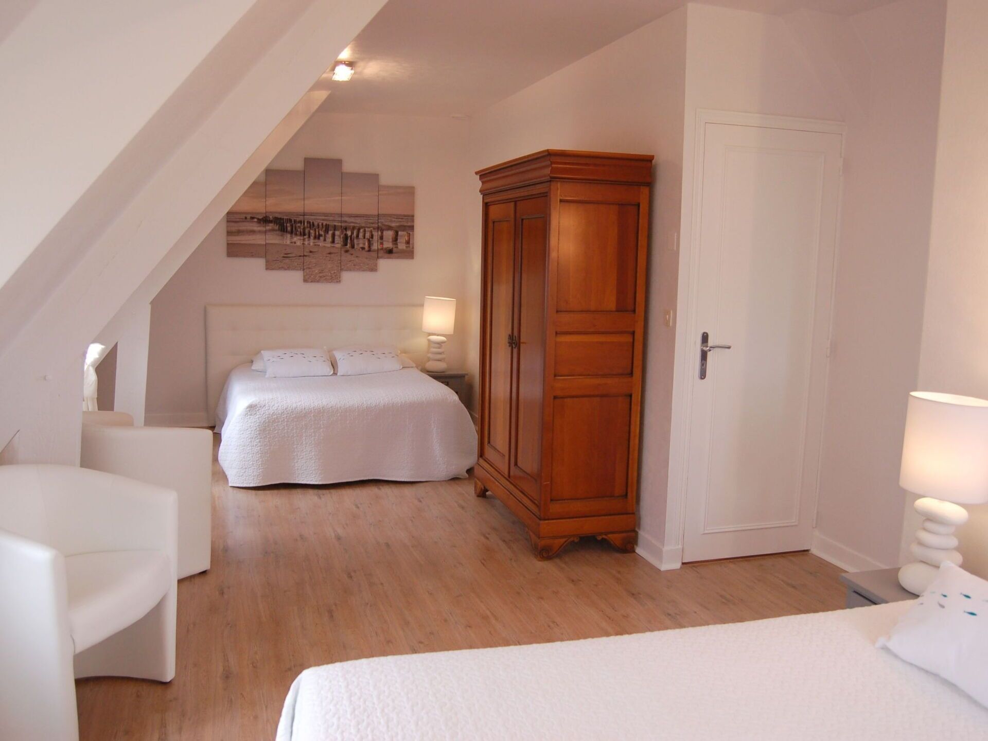 A bedroom with a bed, a wooden wardrobe, a white door, and a white armchair.