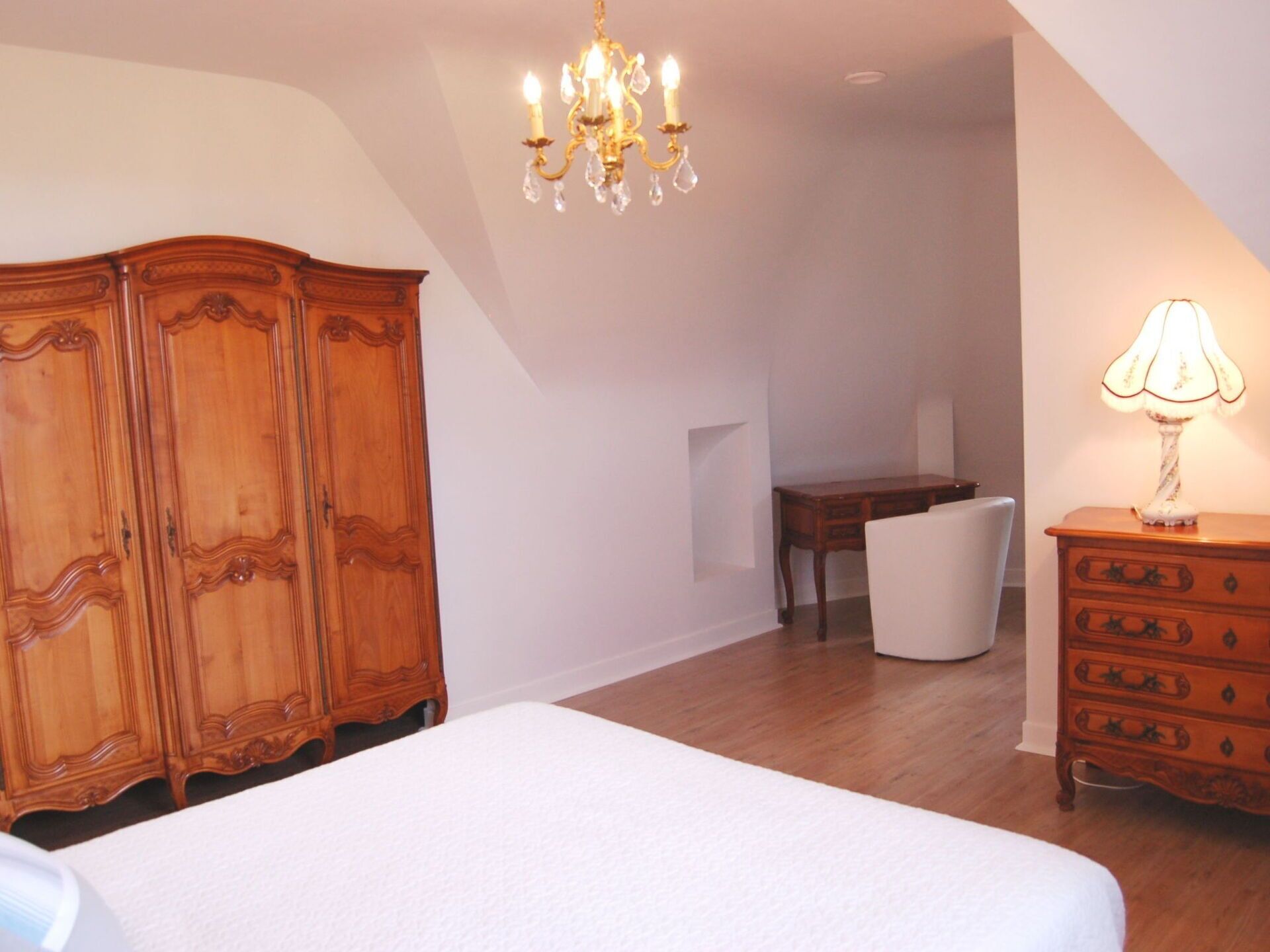 A bedroom with a large bed, wooden wardrobe, a desk, and a dresser.