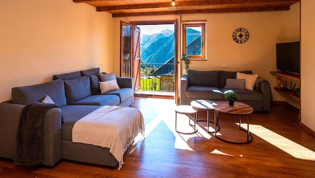 Una sala de estar acogedora con techo de madera, un sofá, un sillón más pequeño y un televisor en un estante.