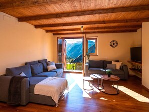 Un salon chaleureux avec un plafond en bois, un canapé, un petit divan et un téléviseur posé sur une étagère.