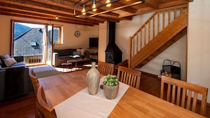 Un salón acogedor con techo de madera, una mesa de comedor con sillas, un sofá, una chimenea y una escalera.