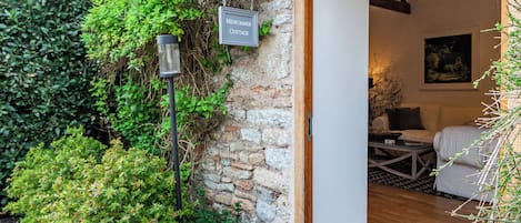 A stone cottage entrance with a sign, a wooden door, and a cozy interior with a sofa and a painting.