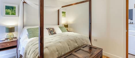 A four-poster bed with a wooden frame, a bedside table with a lamp, and a small wooden chest.