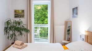 Une chambre d’hôtel avec un lit, une plante en pot, une fenêtre donnant sur un paysage verdoyant et un tableau accroché au mur.